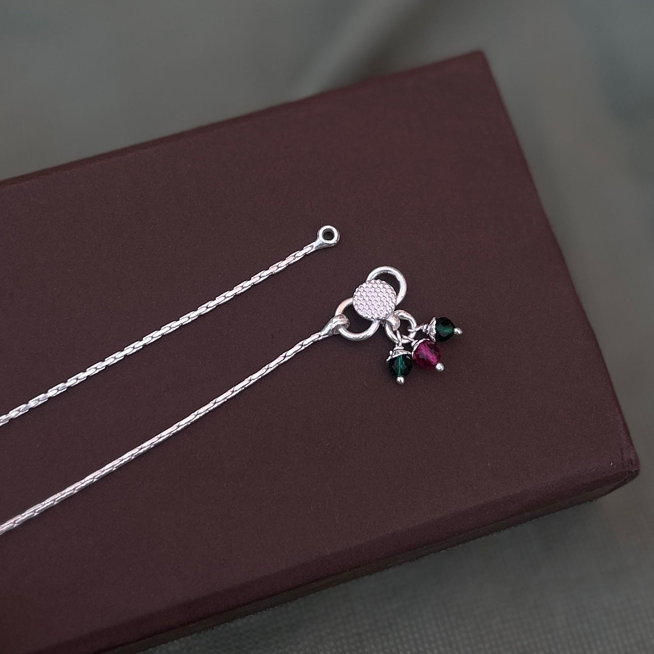 Woman wearing a sterling silver cherry charm anklet with colorful beads and a plain silver anklet."